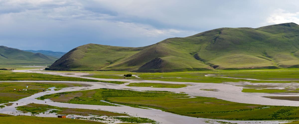 A river winding through a valley with green hills and mountains in the background.