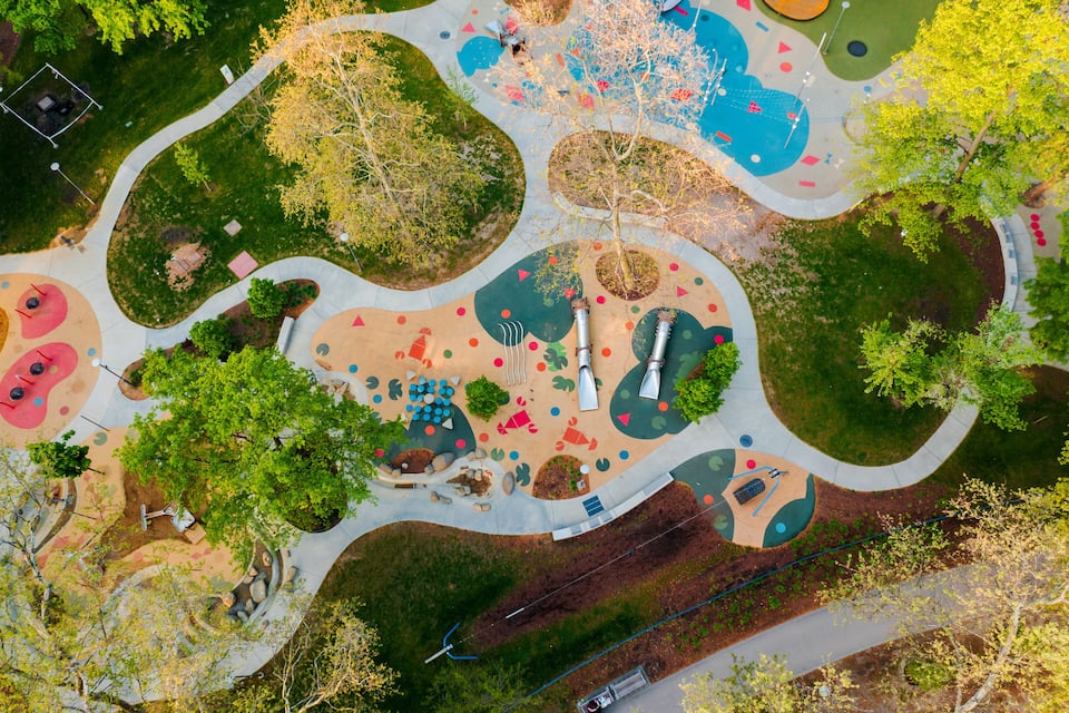 An aerial view of a park with winding paths, playgrounds, and trees.