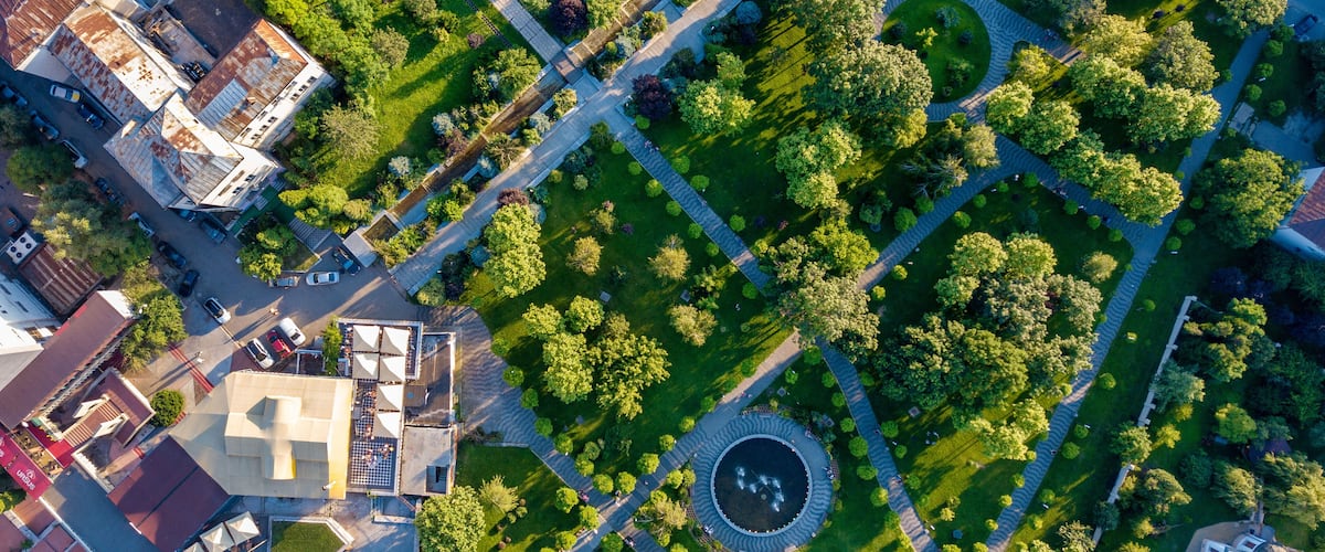 An aerial view of a park with a circular fountain, pathways, and surrounding greenery.