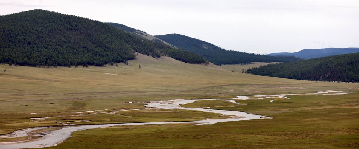 A river winding through a grassy valley with forested hills in the background.