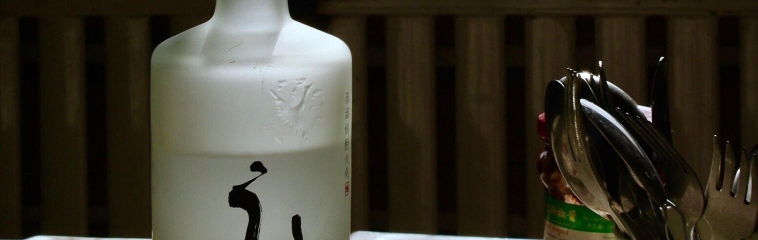 Una botella con caligrafía y texto coreano, un tazón y una ventana que da a un paisaje nevado.