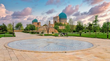 A courtyard with a patterned floor, a gazebo, and a mosque with two domes in the background.