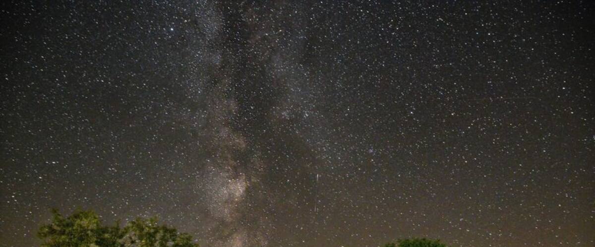 A night sky filled with stars, a wooden cabin, and two tents in a grassy field.