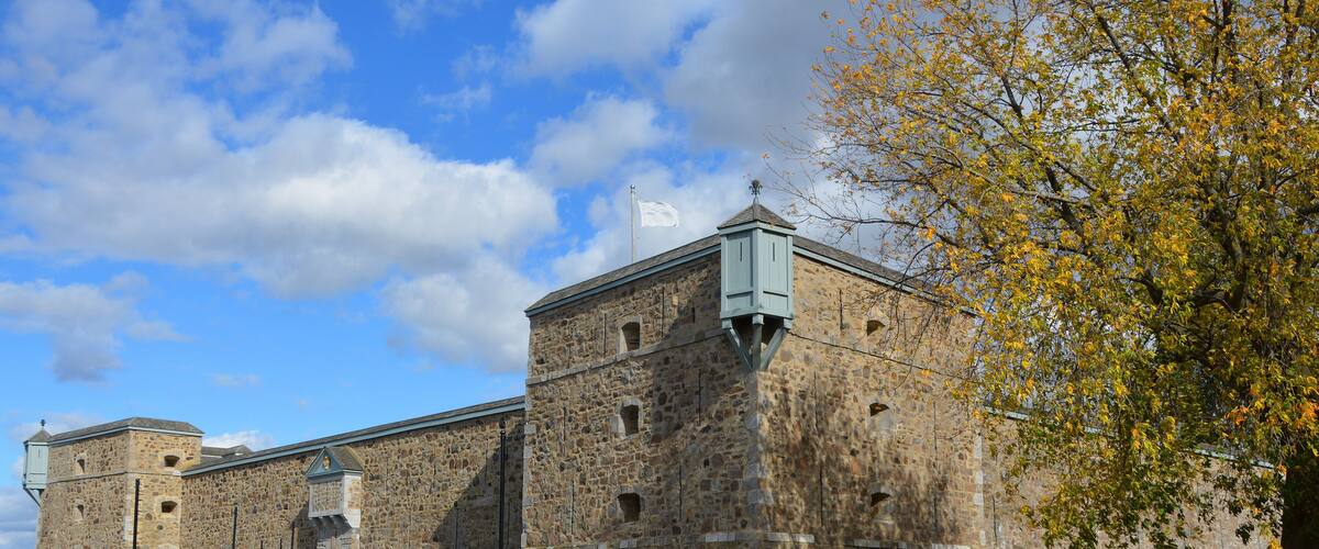 A historic stone building with a flagpole, a flag, and a tree with autumn leaves.
