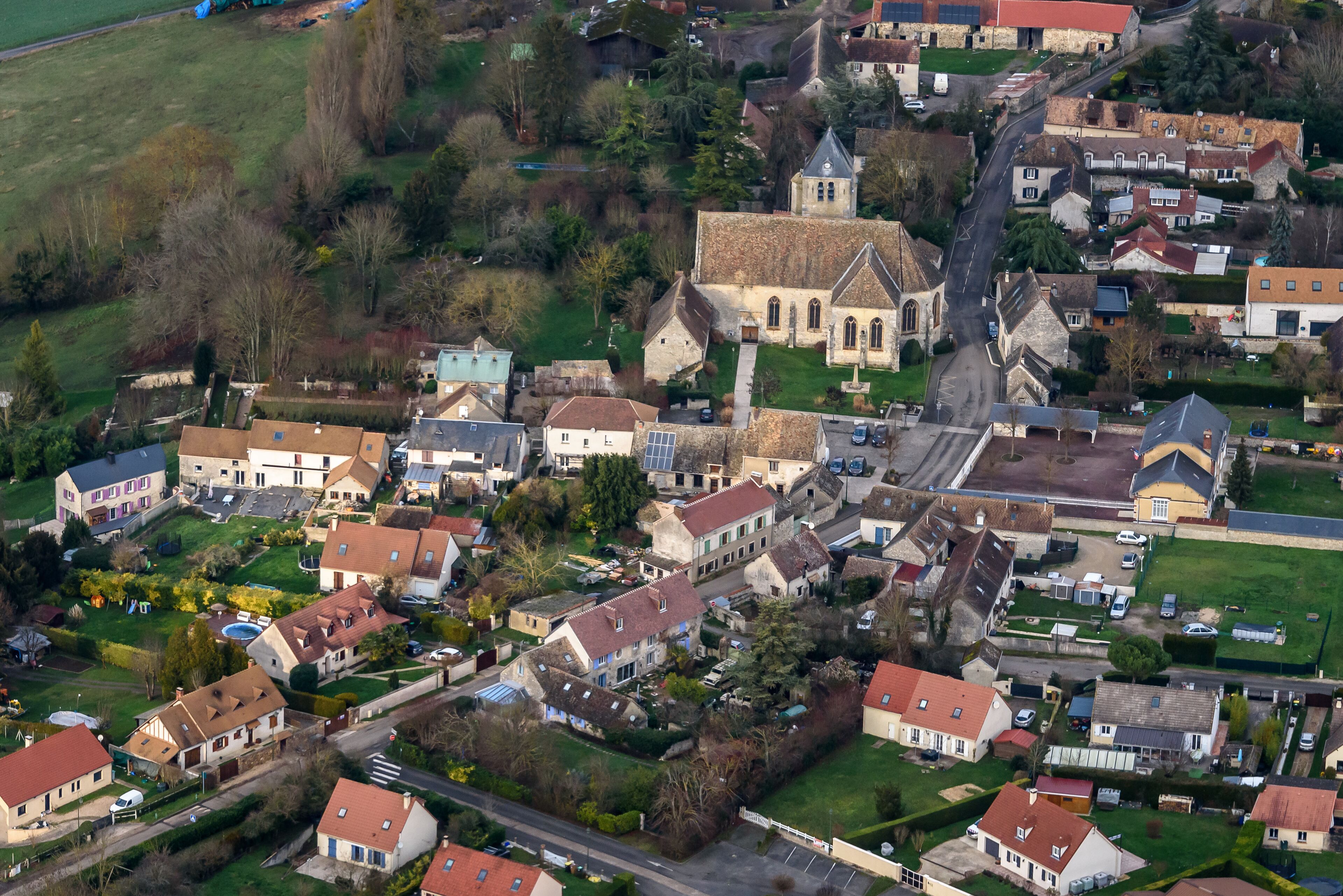 An aerial view of a small village with a prominent church, residential houses, and green spaces.