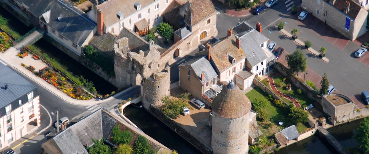An aerial view of a historic town with a prominent tower, narrow streets, and a river.