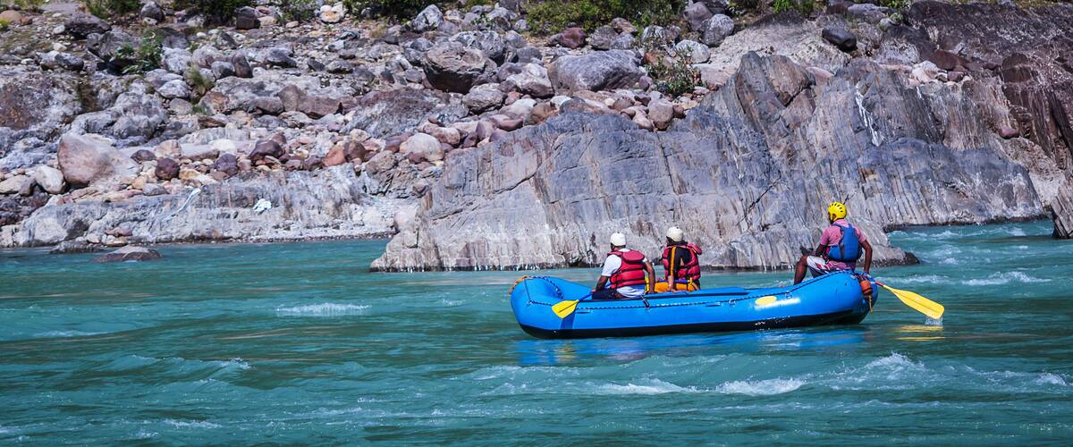 A blue raft with two people paddling on a river surrounded by rocky terrain.