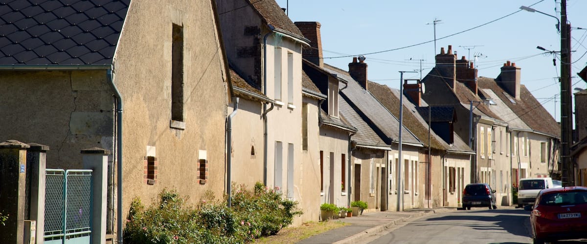 A residential street with houses, a red car, and a clear blue sky.