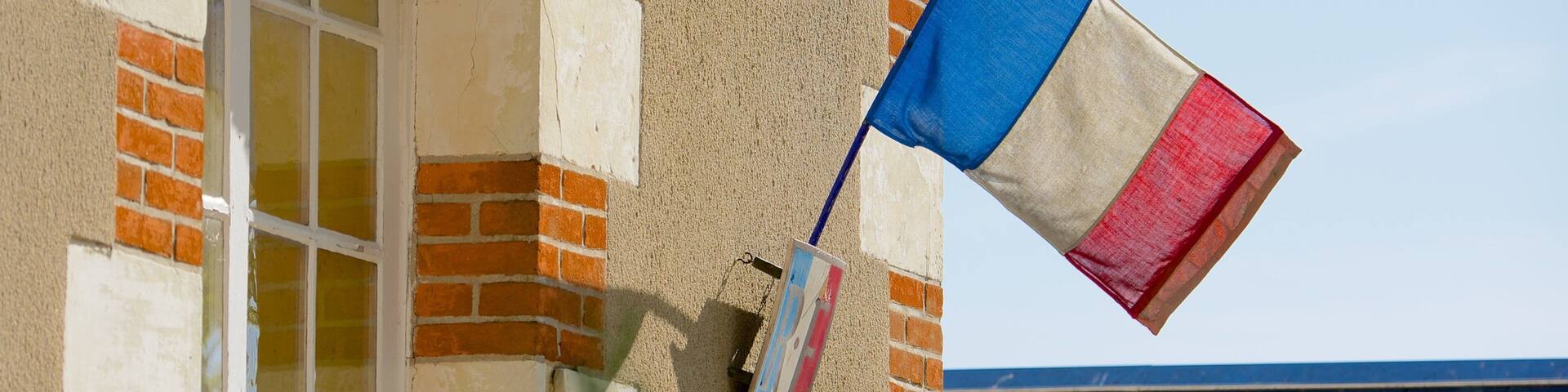 A building with a French flag, a window, and a blue roof.