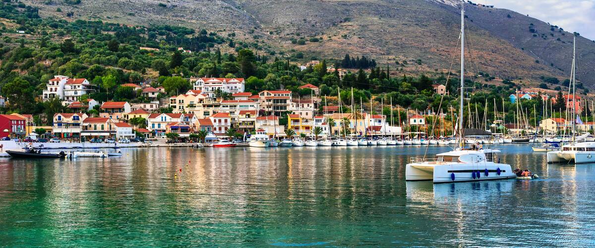 A coastal town with colorful buildings, a marina with boats, and a mountainous backdrop.
