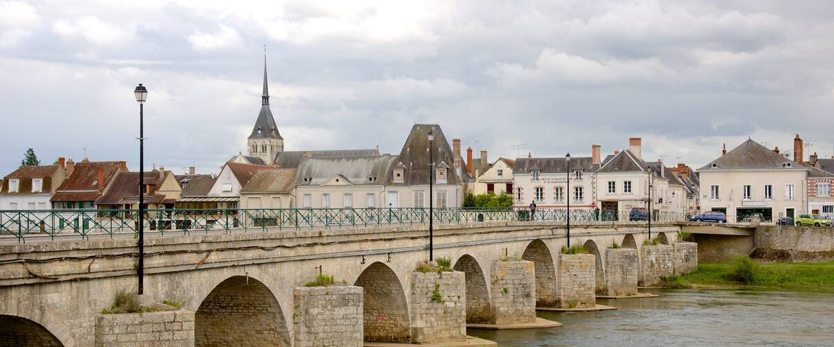 A stone bridge over a river with a church spire in the background.