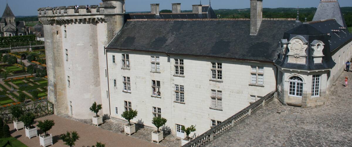 A historic castle with a large tower, a courtyard with trees, and a cobblestone pathway.