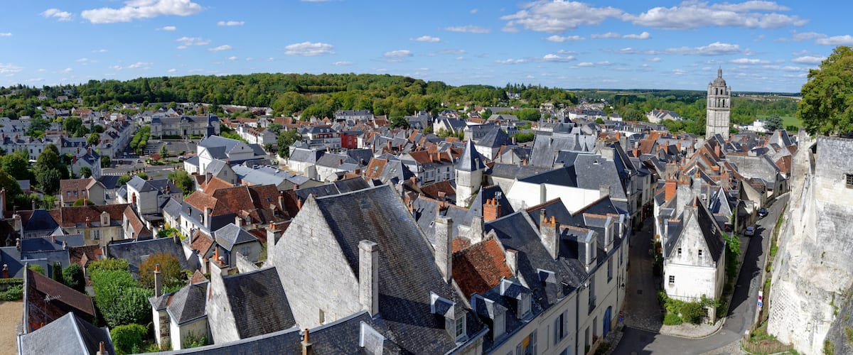 A historic town with a prominent tower, dense architecture, and a green hill in the background.