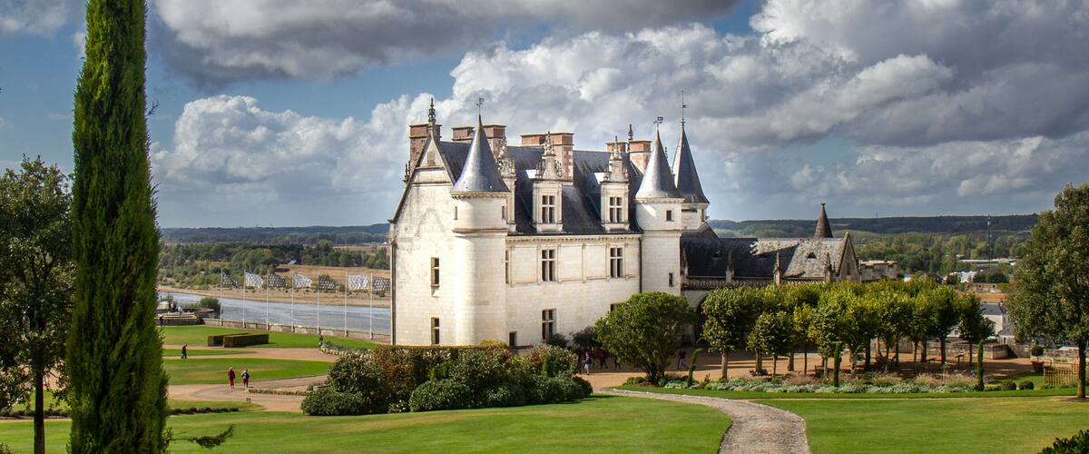 A historic castle with multiple towers, surrounded by lush greenery and a river.