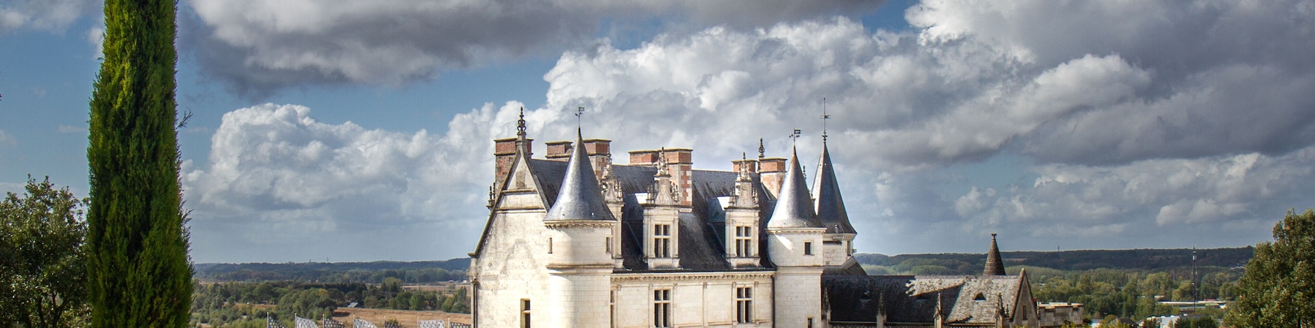 A historic castle with multiple towers, surrounded by lush greenery and a river.