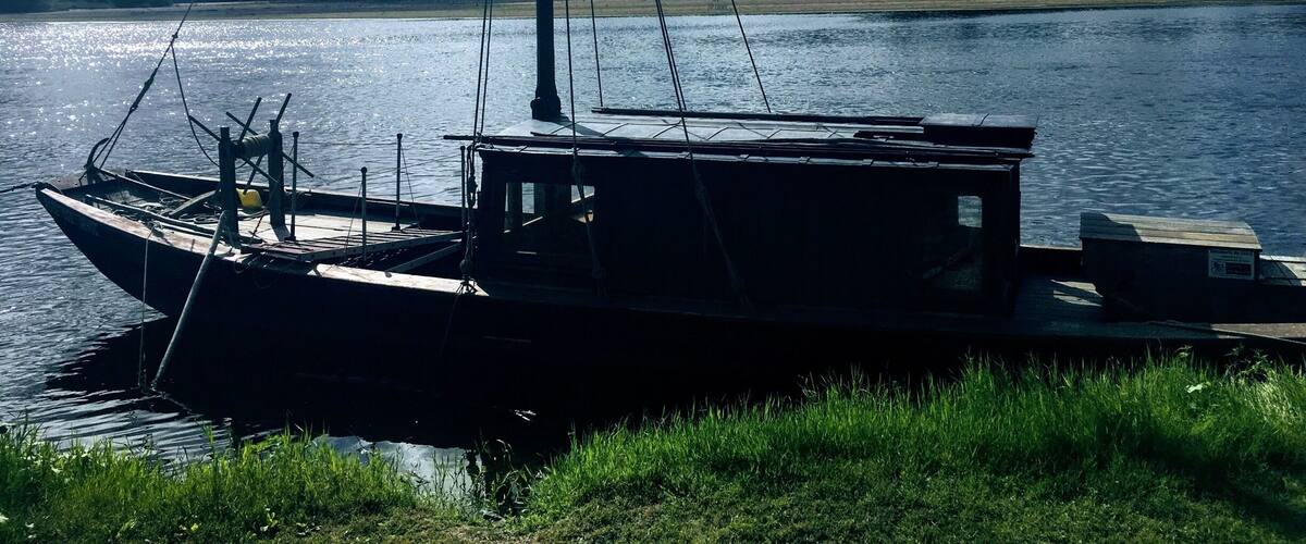 A sailboat docked at a grassy riverbank with a cloudy sky in the background.