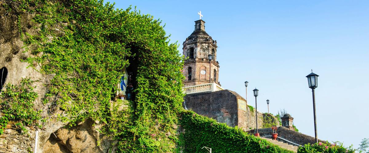A stone staircase leading up to a church with a bell tower, surrounded by greenery.