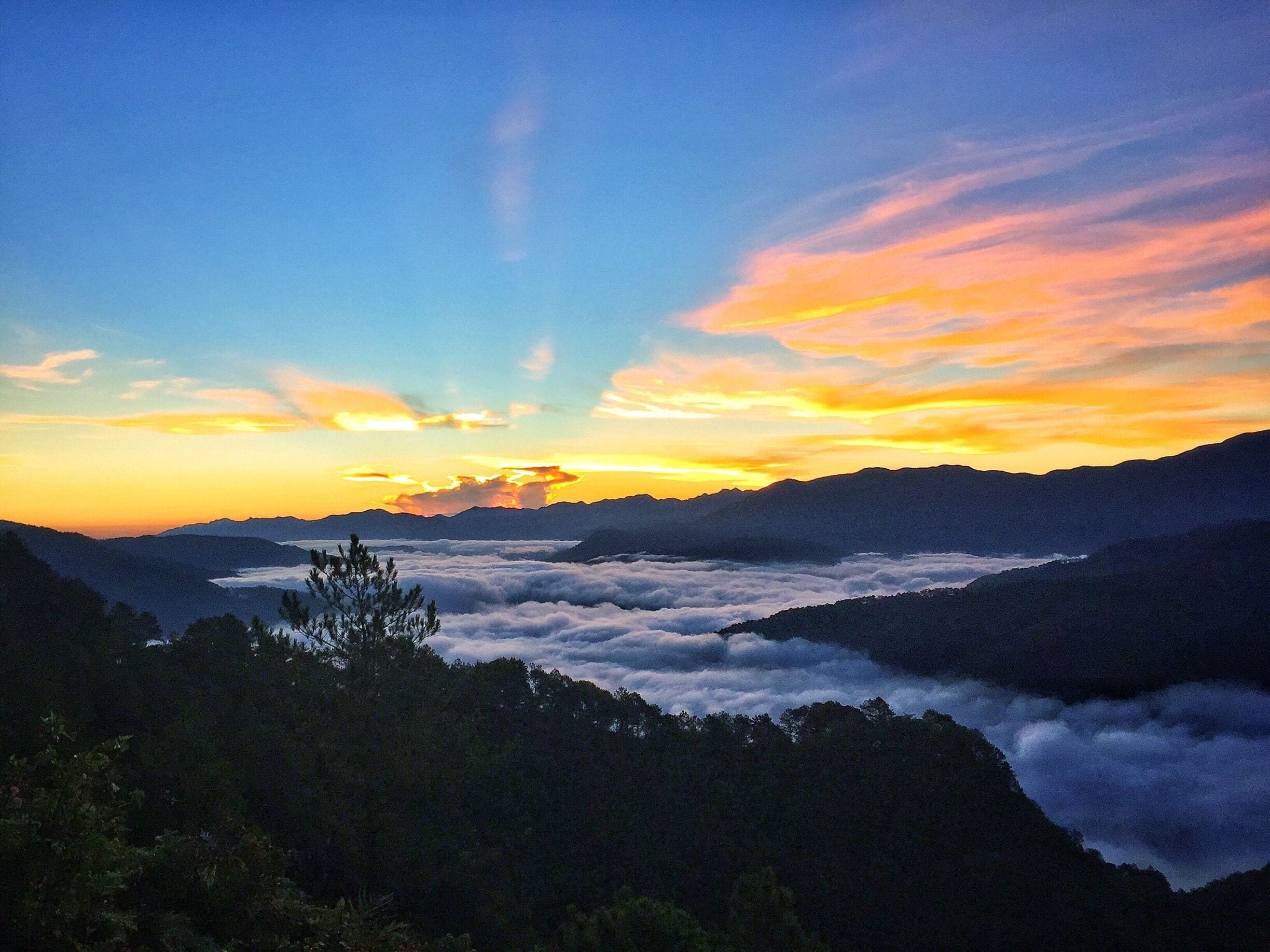 A mountain landscape at sunset with clouds below the peaks and a clear sky above.