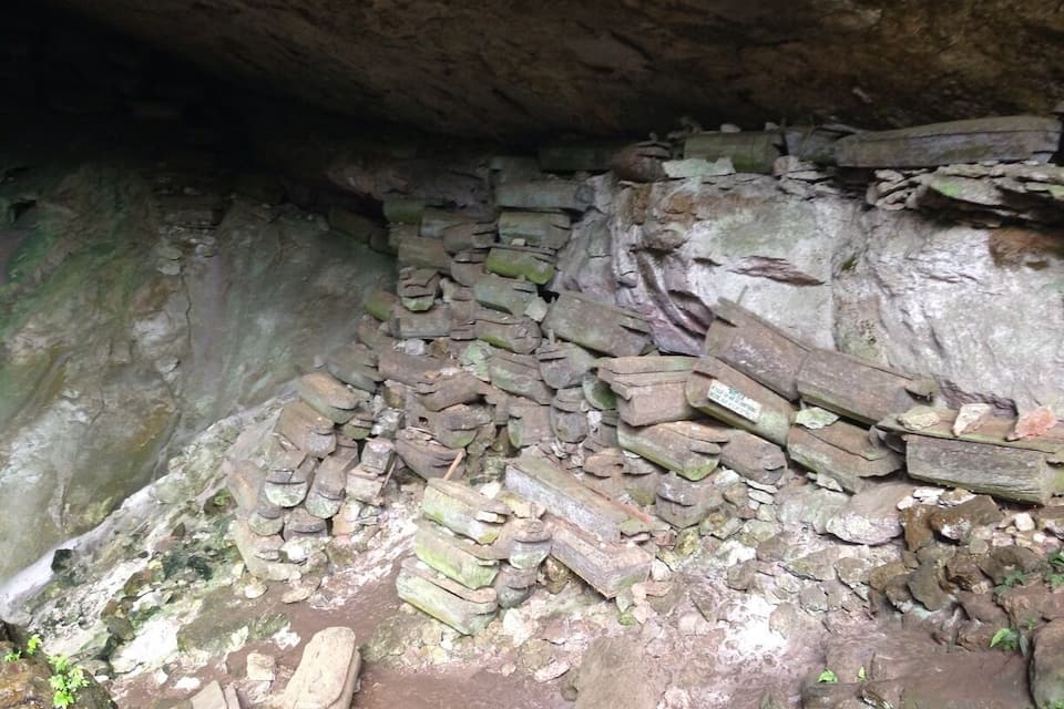 Interior de una cueva con paredes de piedra y algunas tablas de madera dispersas.