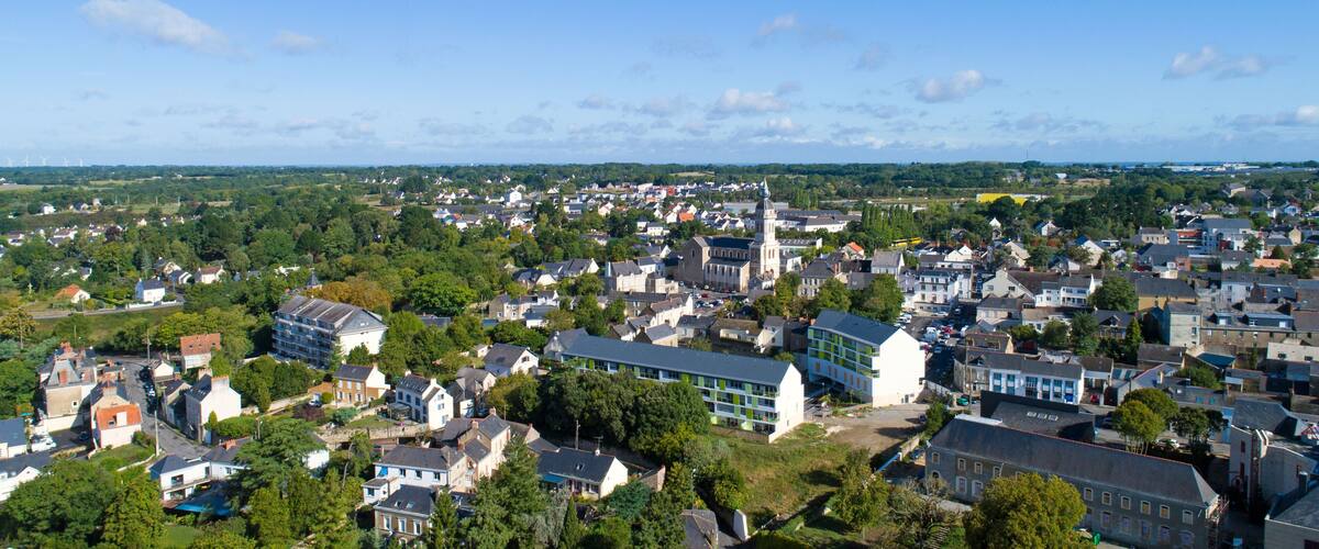 A town with a prominent church steeple, dense residential buildings, and surrounding greenery.