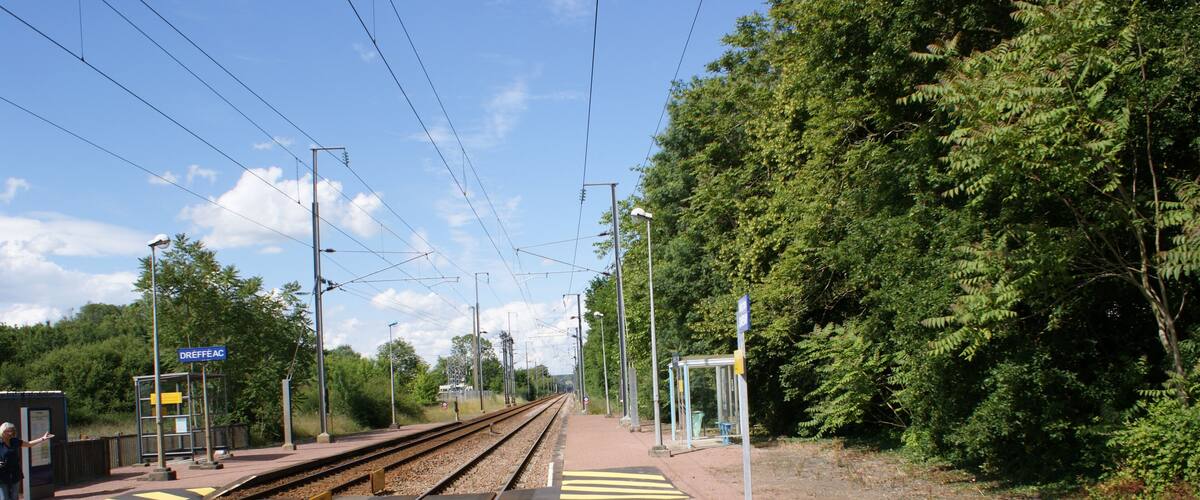 A railway platform with tracks, overhead wires, and a shelter.
