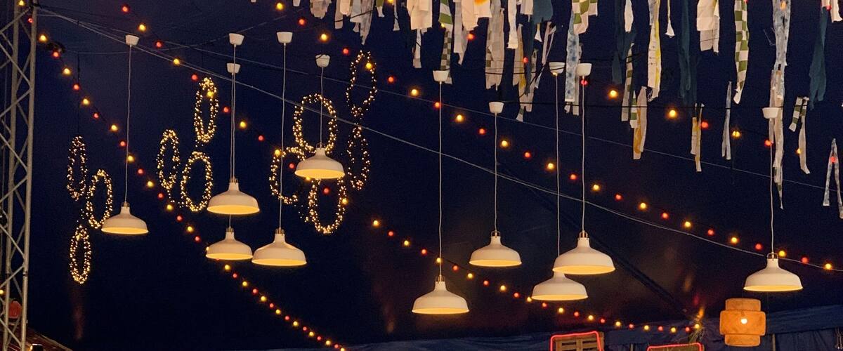A street food festival with tables and chairs, string lights, and hanging clothes.