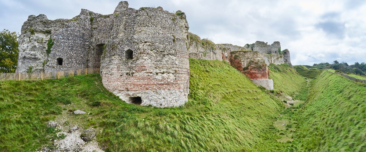 A historic stone castle on a grassy hill with a cloudy sky.