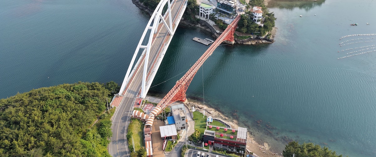 A large suspension bridge spanning a river, surrounded by lush greenery and a small island with buildings.