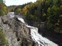 Une cascade d’eau se précipitant le long d’une falaise rocheuse, entourée d’arbres aux couleurs automnales.