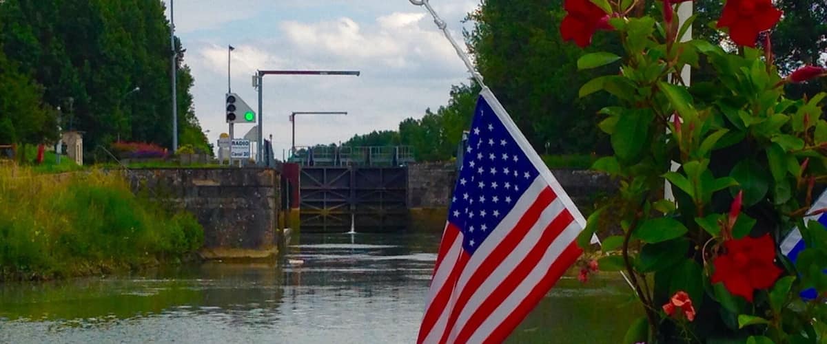 A river with an American flag, a lock gate, and a radio tower in the background.