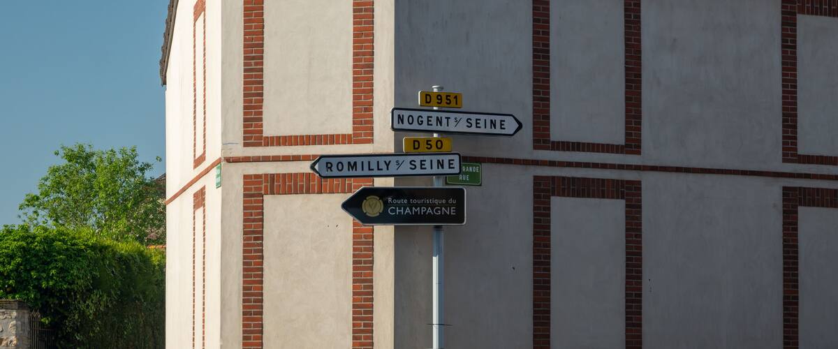 A building with a signpost indicating directions to Nogent-sur-Seine, Romilly-sur-Seine, and Champagne.