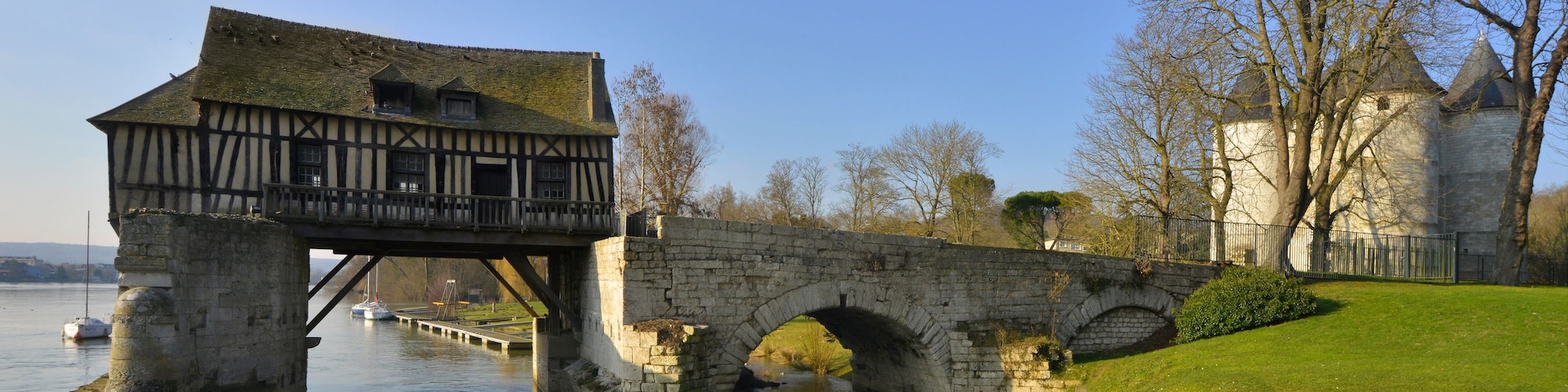 Un puente de piedra sobre un río, un castillo con una torre y una orilla cubierta de hierba.