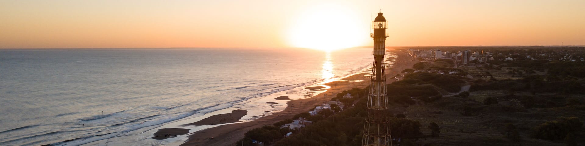 Aerial shot of the sunset on the beach with a lighthouse on the coast.