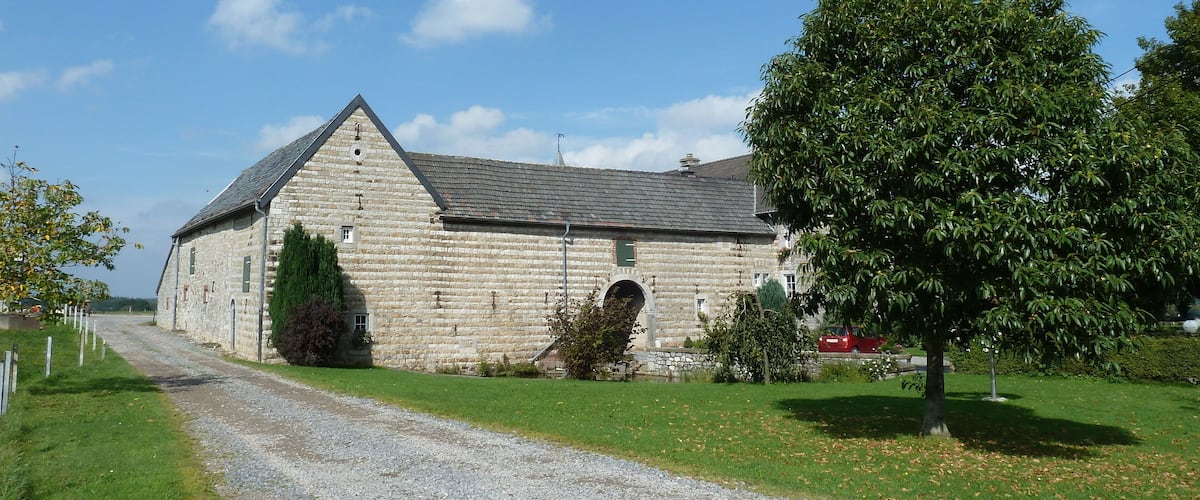 A stone barn with a gravel driveway and a large tree in front.