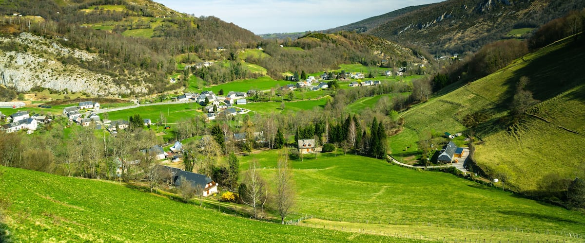 A valley with houses, green fields, and mountains.