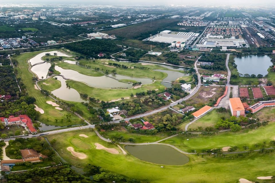 An aerial view of a golf course with multiple water hazards, surrounded by residential and commercial buildings.