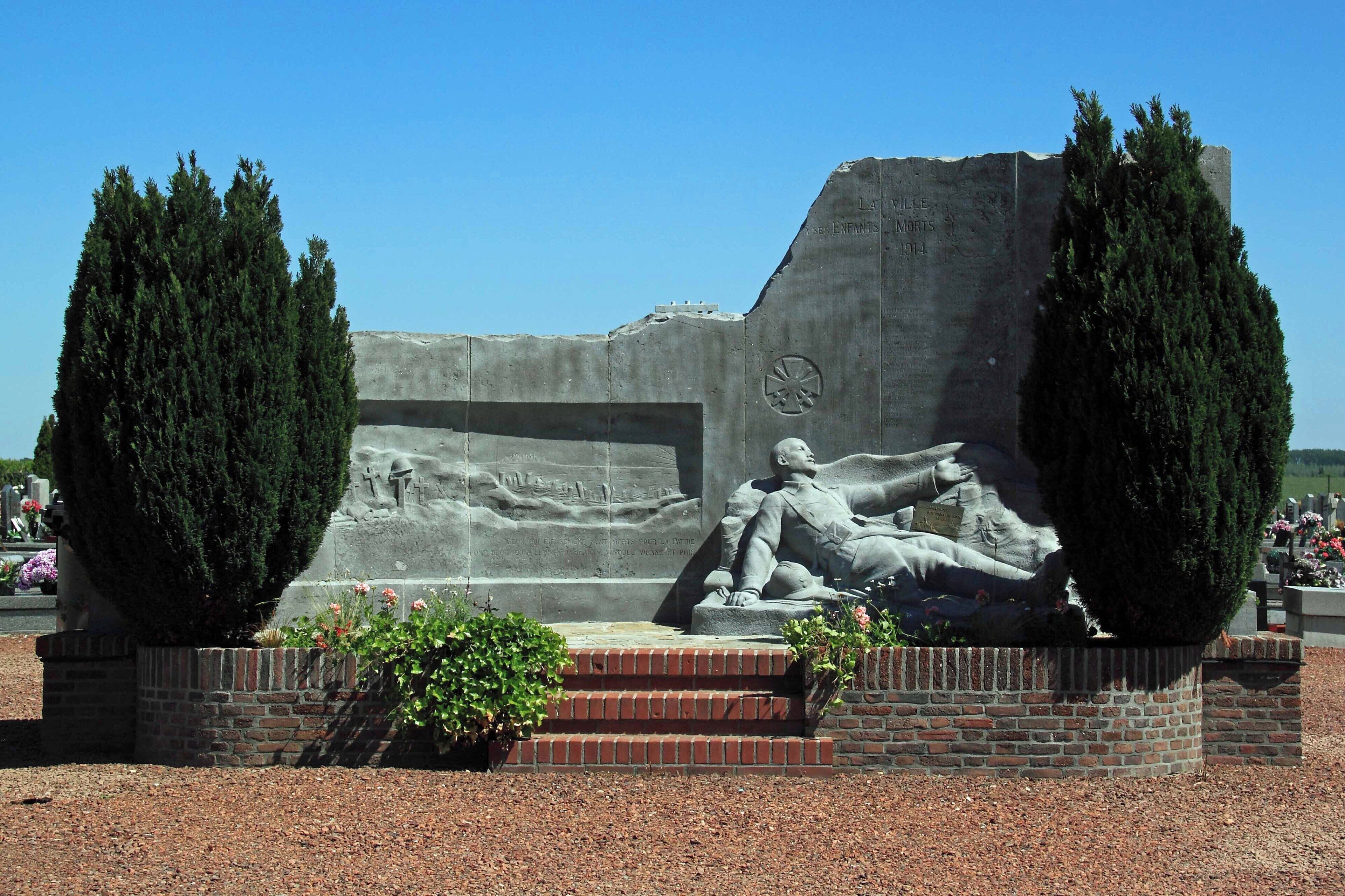 A memorial monument with a reclining figure, two tall trees, and inscriptions.