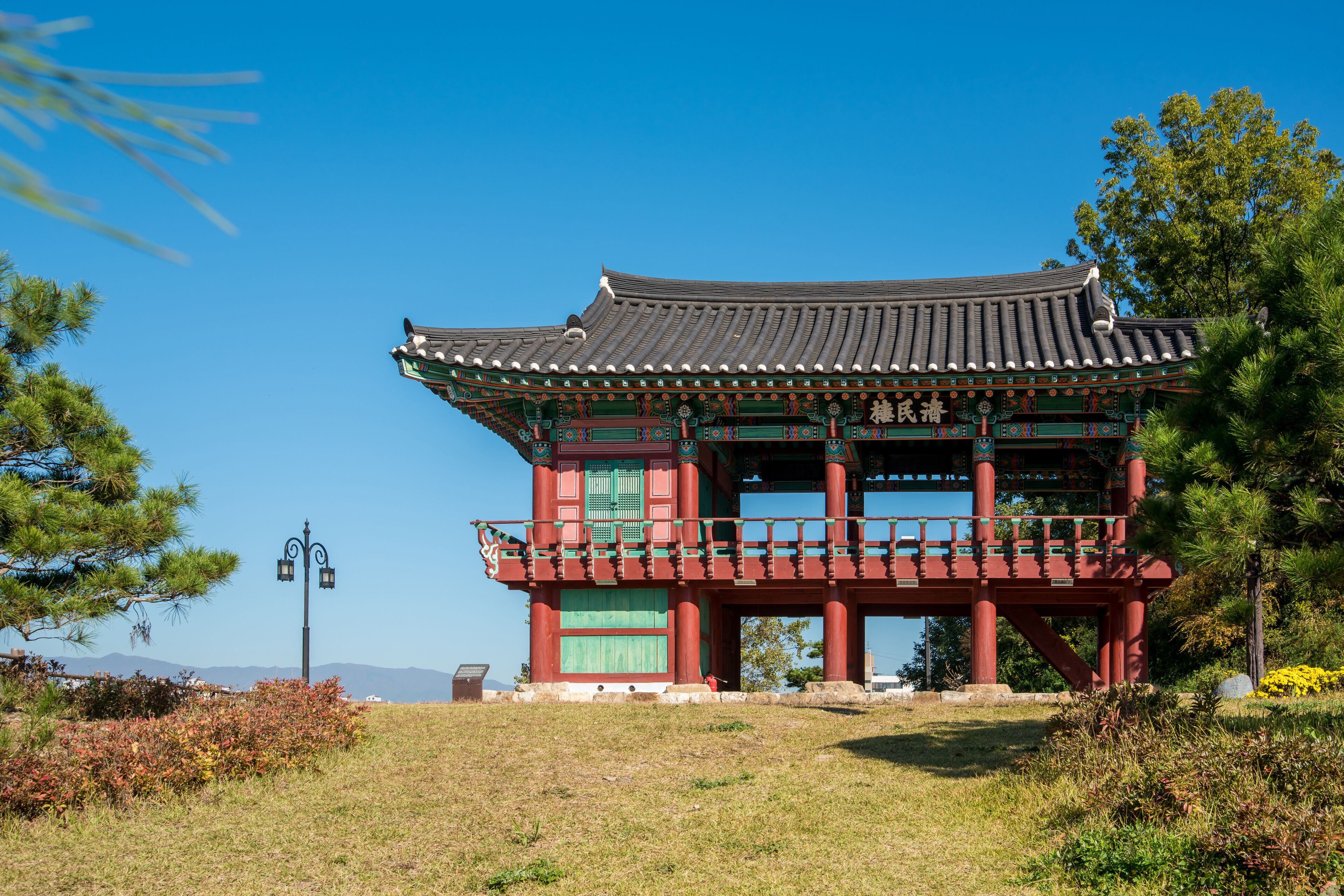 A traditional Korean pavilion with a tiled roof, surrounded by grass and trees.
