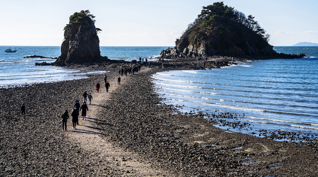 Seung-eon-ri, Anmyeondo Island, Taean-gun, Chungcheongnam-do, South Korea - April 13, 2021: Tourists are walking on sea road at low tide at Kkotji Beach against two rock islands and horizon