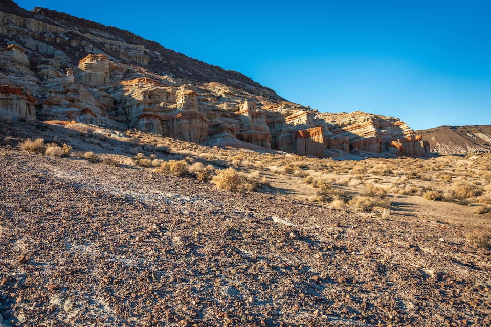 A rocky desert landscape with layered rock formations and sparse vegetation.