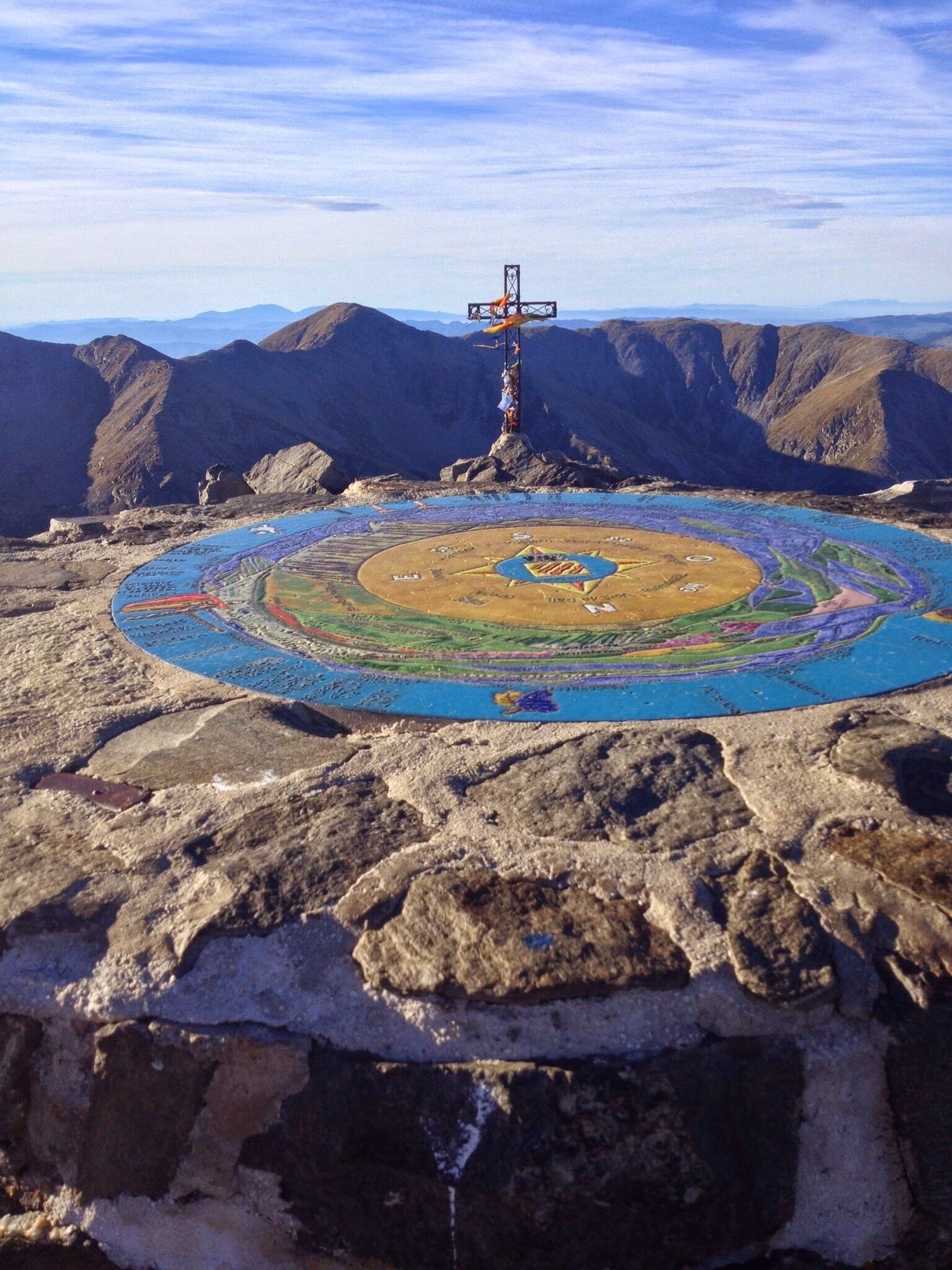 A large, colorful mandala-like design on a rocky surface with a cross structure in the background.