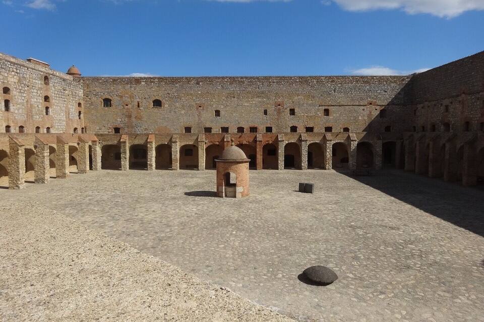A courtyard with stone walls and arches, a central tower, and a clear blue sky.