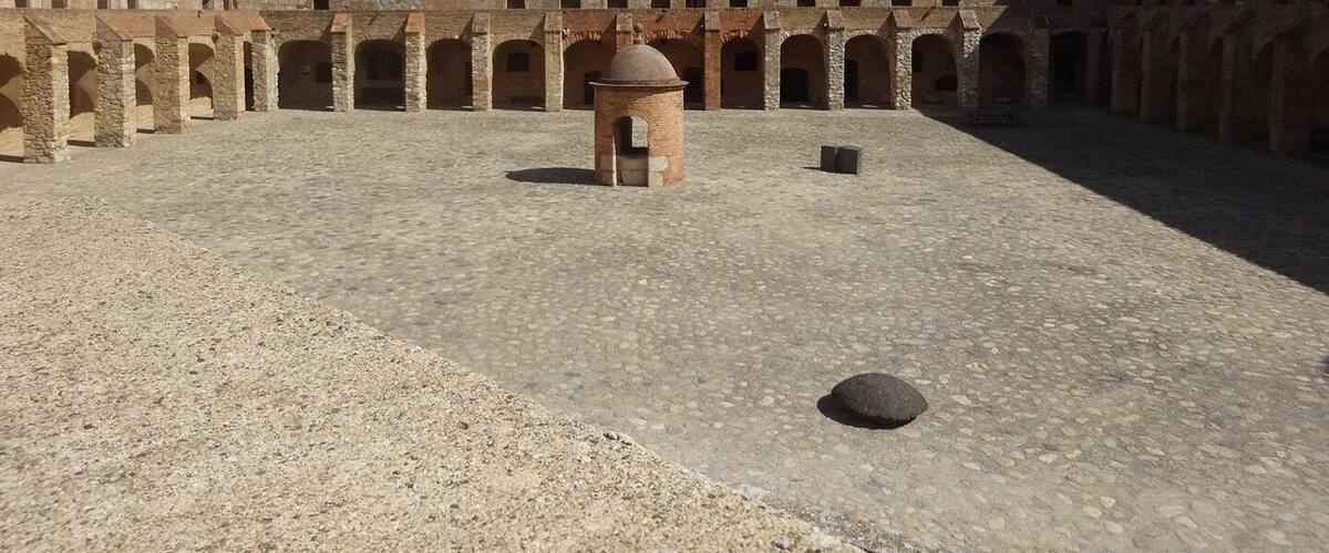 A courtyard with stone walls and arches, a central tower, and a clear blue sky.