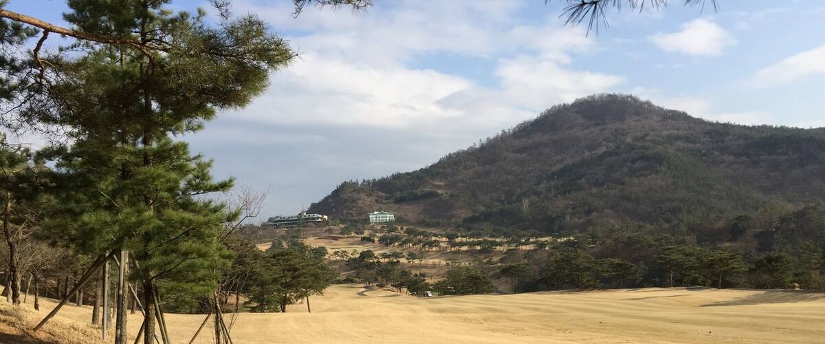 A golf course with a mountain in the background and a building on the hillside.