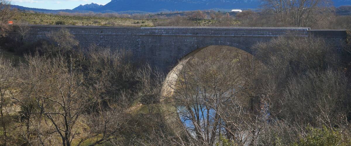 A stone bridge over a river with mountains in the background.