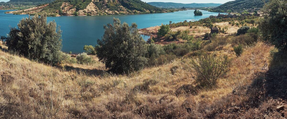 Ein See, umgeben von Hügeln, Bäumen und einem kleinen Dorf.