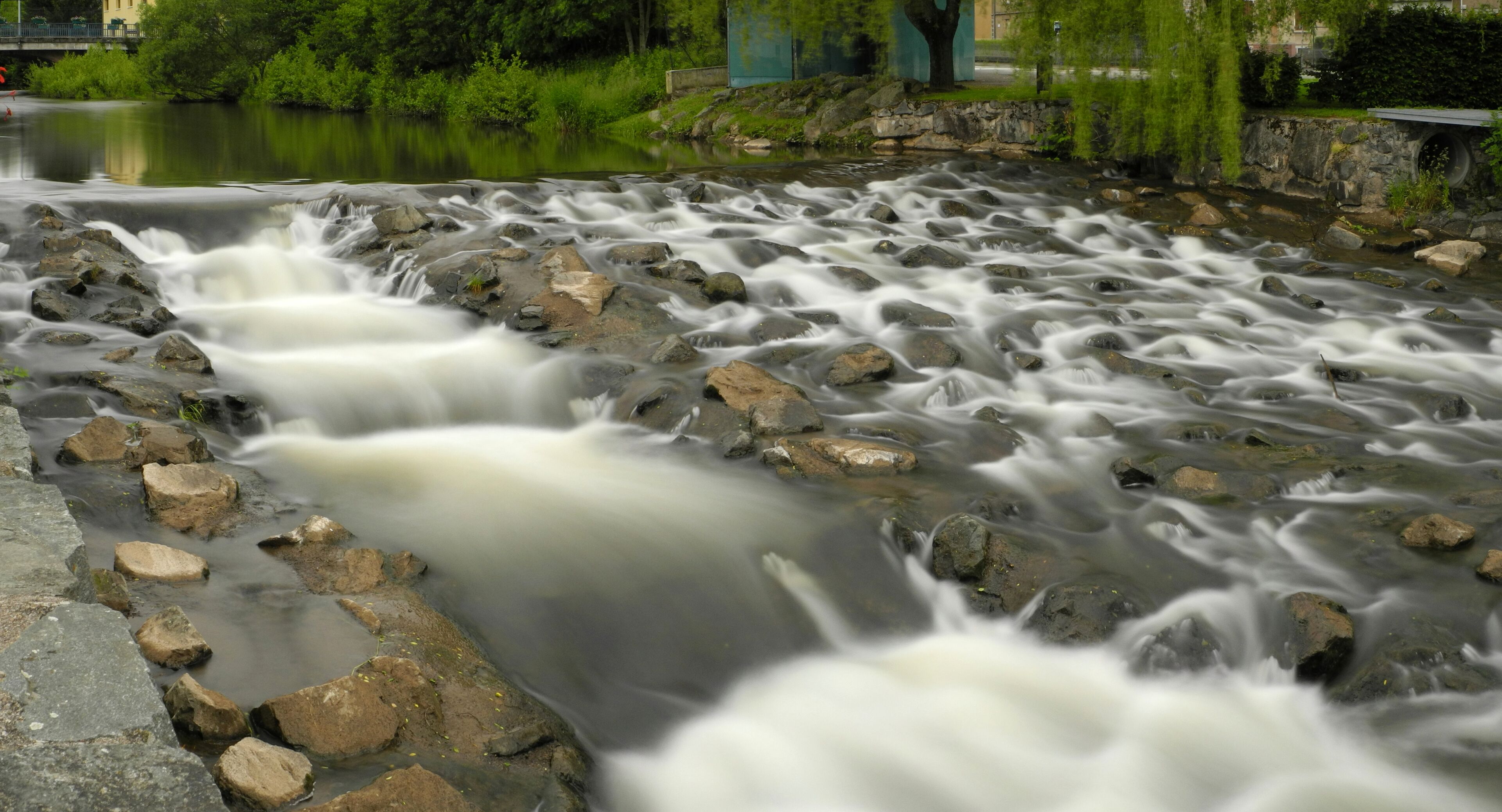 A river with a rocky bed and a bridge in the background.