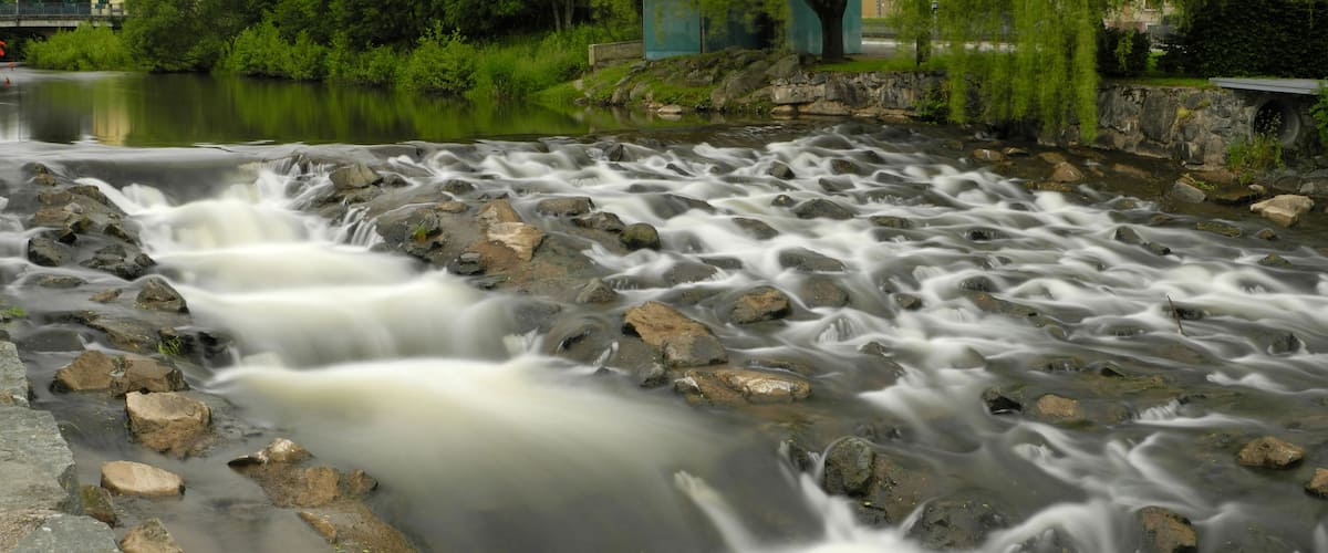 A river with a rocky bed and a bridge in the background.
