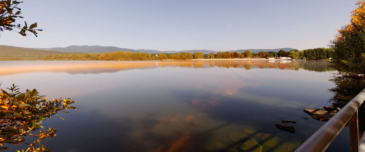 A calm lake with reflections of trees and mountains in the background.