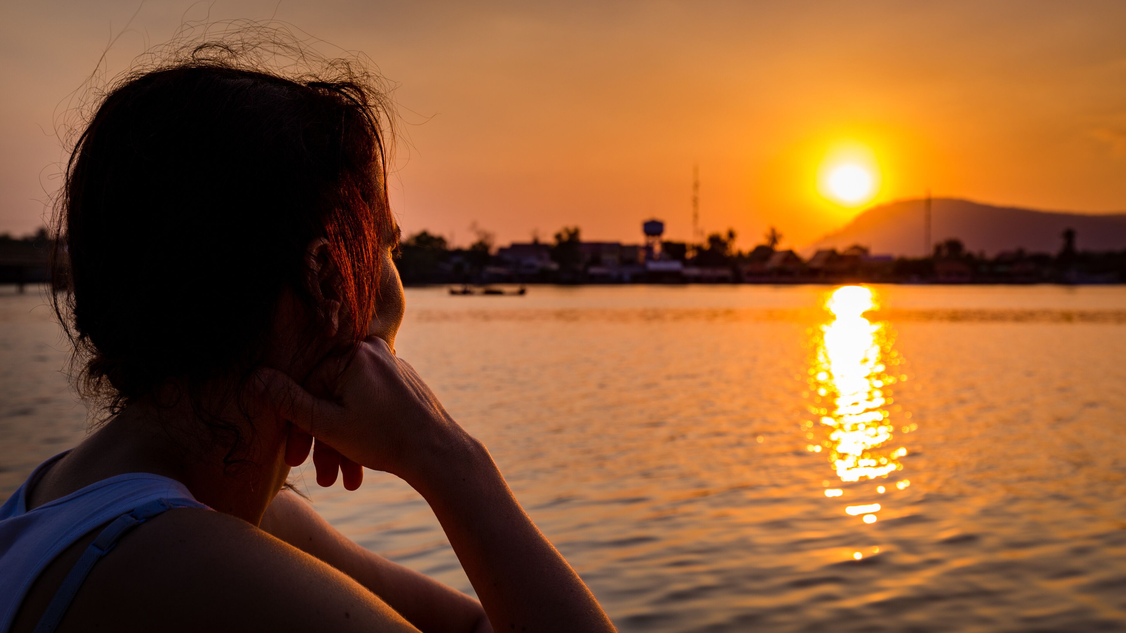 A sunset over a body of water with a silhouette of a person and distant buildings.
